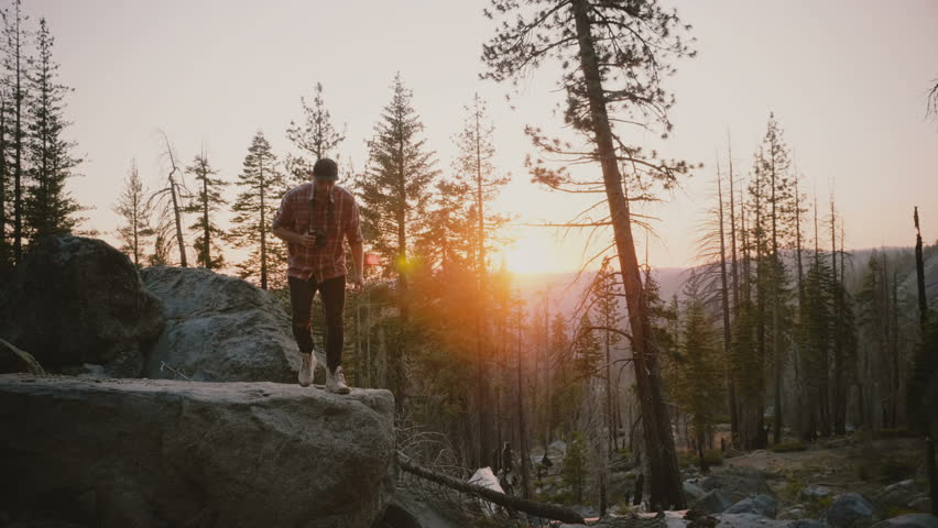 Successful young male blogger jumping off a big forest stone, hikes on rocks at amazing Yosemite park sunset slow motion