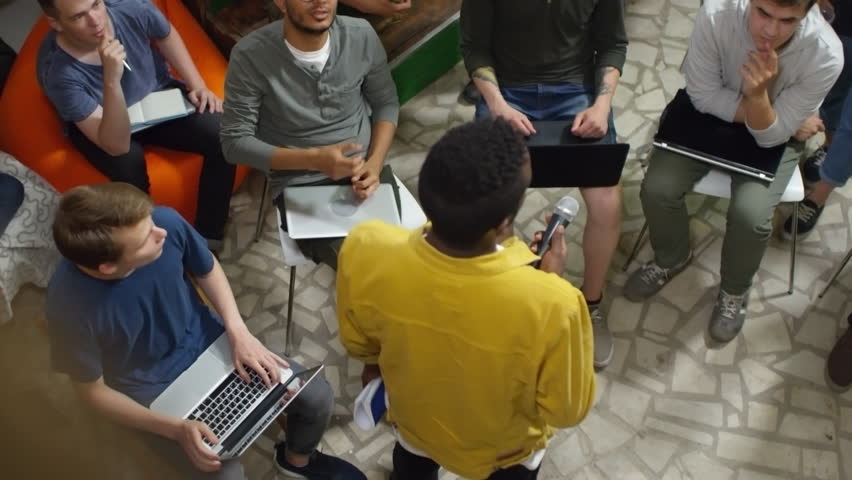 High angle view of young black man delivering presentation at workshop, group of listeners discussing topic with him