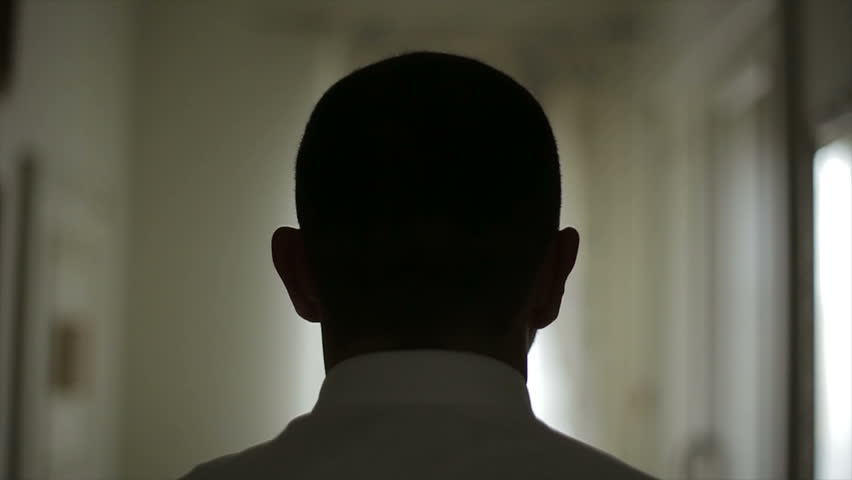 Close-up of a Man in white shirt opening white door. Man pushes the door, enters a long corridor and walks towards a window.