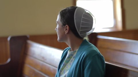 A portrait of a young Mennonite woman looking out a church window.