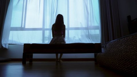 little teenager looking out of the window in bad weather, silhouette of a fragile teenager girl on the background of a large window