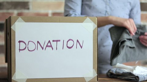 Volunteer is puting clothes to cardboard box for donation