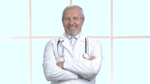 Cheerful male doctor with arms crossed. Smiling senior doctor on clinic window background, portrait. Face of happy doctor.