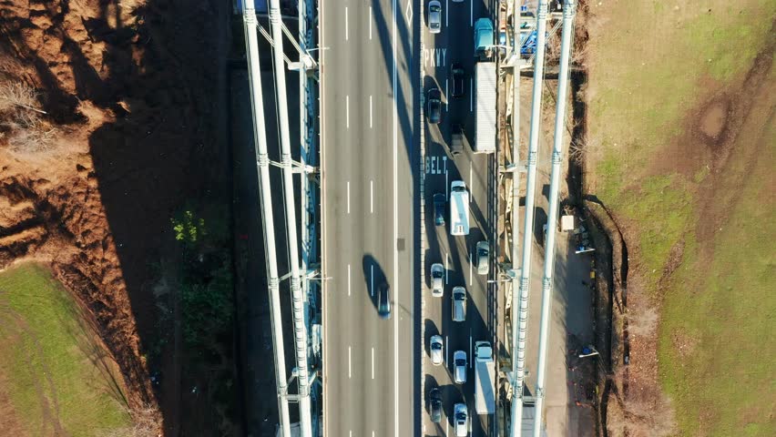 Aerial drone footage of Verrazzano Narrows Bridge, centered above the highway, with view towards Brooklyn (uptilt movement)