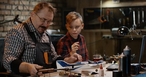 Grandfather and grandson in the garage soldering the model of a toy airplane with the radio control