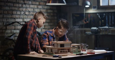Medium shot of two boys repairing a model house in a garage