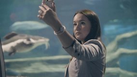 Beautiful woman making mobile selfie photo on background fish in oceanarium