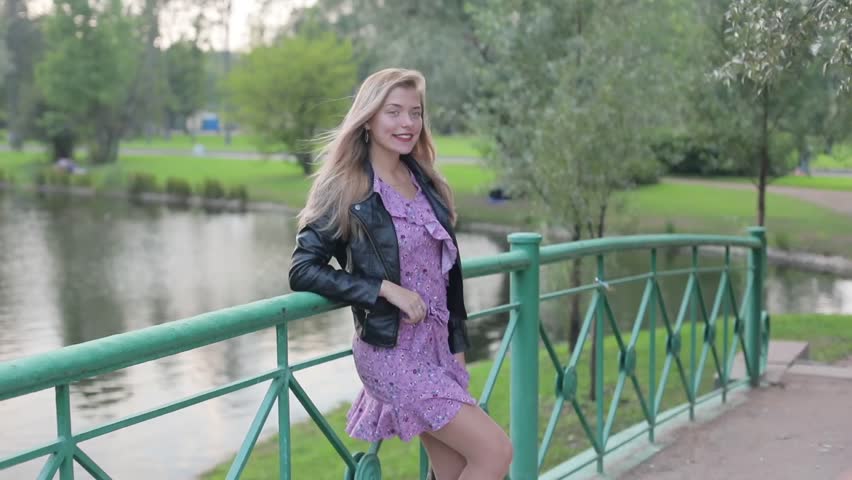 Young people do a photo session on the mobile in the park on the bridge near the pond.