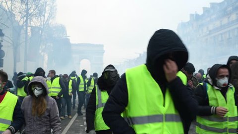 Paris, France - December 8 2018: Protesters protect and run away for cover from tear gas launched by riot police during a Yellow Vests (Gilets jaunes) protest against living costs and rising prices 