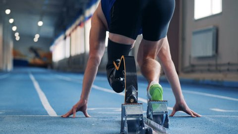 A man sprints, wearing prosthetic leg, back view.