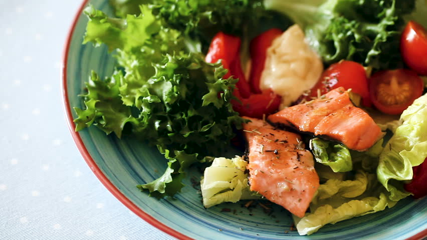 Close up of cooked egg with  fried trout, vegetables and  fresh lettuce at plate on table