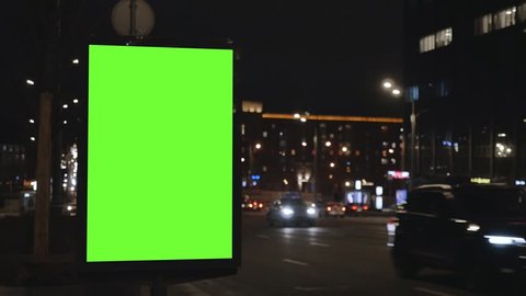 close city light vitrine with empty green screen on roadside against cars driving along night street