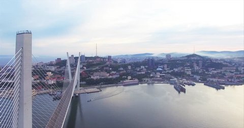 Amazing ascending aerial view of magnificent sunrise above Vladivostok and Golden bridge across Golden Horn bay. Cityscape and ships moored in the bay. Russia