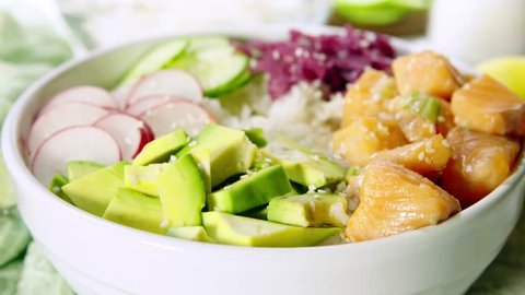 Poke bowl, traditional Hawaiian raw fish salad with rice, avocado, cucumber and radish on bright background. 4K