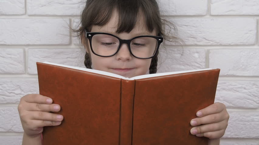 Sticking out tongue. Girl with bangs sticking out her tongue while reading book. Smart child with a book.