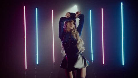 Attractive young blonde woman in a blue costume dancing in a studio with lit neon light. Seductive beautiful moves of a professional female dancer. Shoot with RED RAVEN camera.