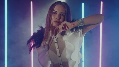 Portirat of attractive brown-haired woman dancing in room with smoke, pink and blue neon lights around. Beautiful young girl showing dancing skills. Shoot with RED RAVEN camera.