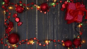 Top view flatlay beautiful Christmas background. Different red ornaments, present gift box and led lights shining isolated on wooden brown background. Real time 4k video footage.