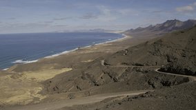 Aerial (10 bit HLG UNGRADED ) of a long beach and a mountain range. Island of Fuerteventura neaf Cofete. UHD Video Footage