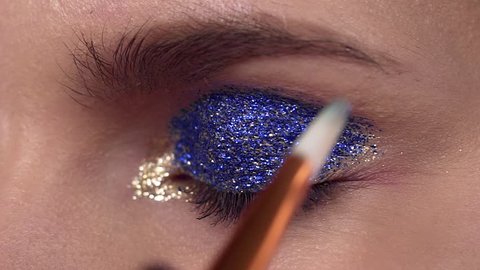 Glitter are applied to the woman's eyelid, making of the evening makeup, eyes makeup, makeup artist's work, close up makeup