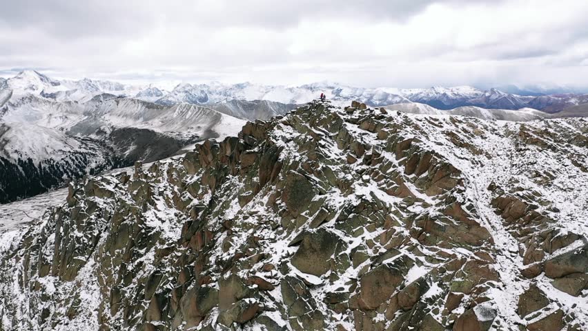 Aerial, orbit, drone shot, around people standing on the top of a snowy mountain, first snow in Rocky mountains national park, on a cloudy, fall day, in Colorado, USA