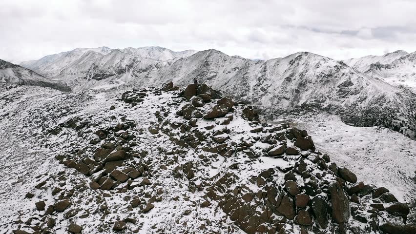 Aerial, orbit, drone shot, around people standing on the top of a snowy mountain, first snow in Rocky mountains national park, on a cloudy, fall day, in Colorado, USA