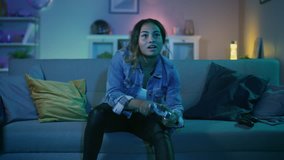 Beautiful Excited Young Black Gamer Girl Sitting on a Couch, Playing and Winning in Video Games on a Console. She Plays with a Wireless Controller. Cozy Room is Lit with Warm and Neon Light.