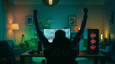 Back Shot of a Gamer Playing and Winning in First-Person Shooter Online Video Game on His Powerful Personal Computer. Room and PC have Colorful Neon Led Lights. Cozy Evening at Home.