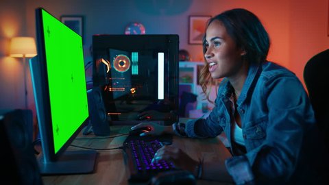 Green Screen Mock Up of an Excited Black Gamer Girl Playing and Winning in Online Video Game on Her Computer. Room and PC have Colorful Neon Led Lights. Cozy Evening at Home.