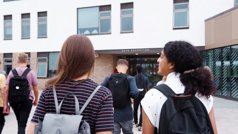 Rear View Of Two Female High School Students Walking Into College Building Together