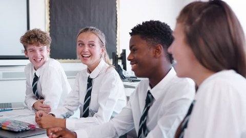 Line Of High School Students Wearing Uniform Sitting At Desk In Classroom Laughing