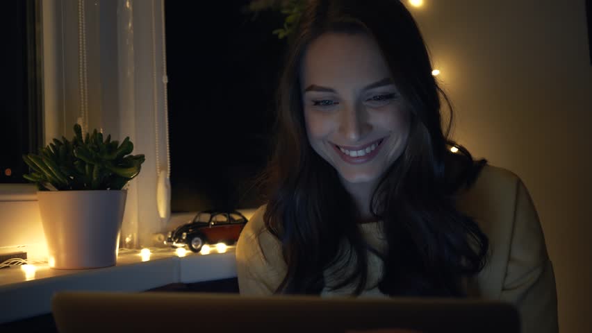 Young beautiful woman smiling while using laptop computer, watching movies and videos while sitting near the window at night. Internet, social network. Close up Royalty-Free Stock Footage #1020765499