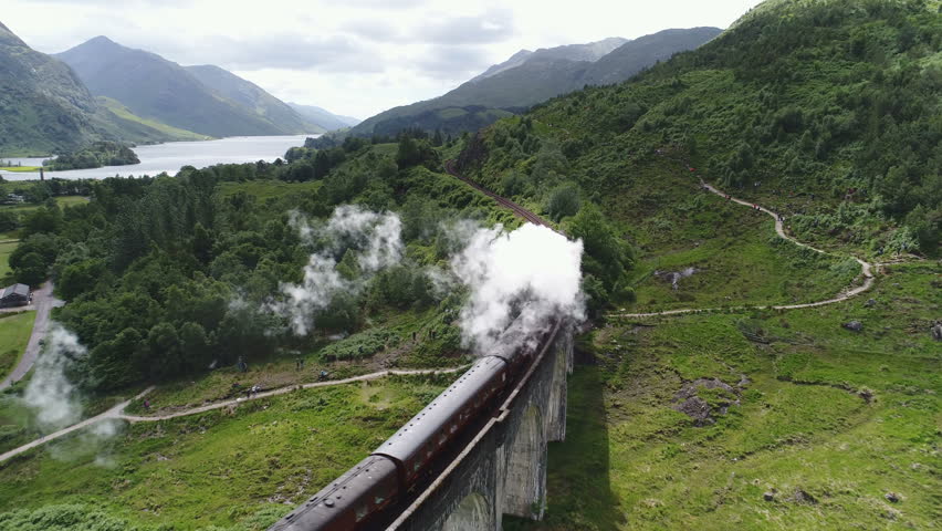 Beautiful drone flight tracking historic steam train near the famous Glenfinnan viaduct, among beautiful green mountain landscape in Scotland Royalty-Free Stock Footage #1020769951