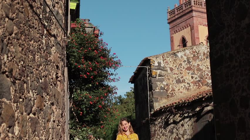 The tourist girl walks through the old streets in rays of the sun