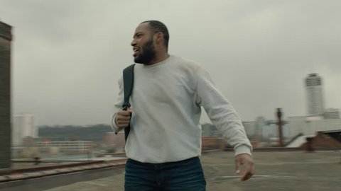Camera spins around black man catching his breath o warehouse rooftop, while his attacker runs to catch up to him in overcast sunlight. Medium shot in 4K with an Alexa Mini camera