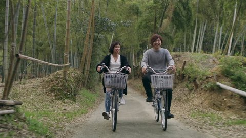 Young Japanese couple riding bikes together through a nature path in a bamboo forest in Kyoto, Japan with soft natural lighting. Wide shot on 4k RED camera.  Video de stock