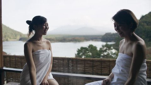 Two relaxed Japanese women sitting on the edge of a hot water bath and looking out to Mount Fuji in the background with soft natural lighting. Medium shot on 4k RED camera. 