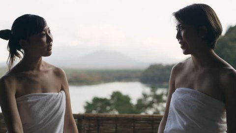 Two relaxed Japanese women sitting and talking on a balcony overlooking the water and Mount Fuji in a traditional spa with soft natural lighting. Close up shot on 4k RED camera.