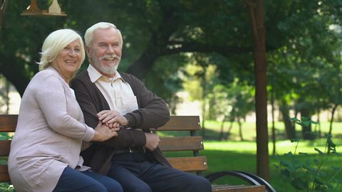 Old couple sitting on bench and happily watching their grandchildren having fun