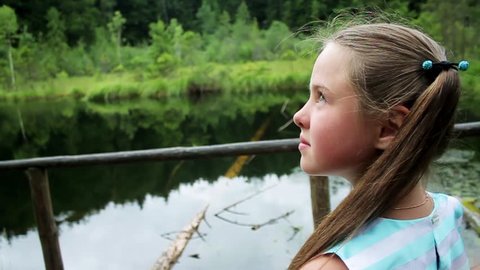 Close up view of lovely smiling little girl standing by the pond in woods, enjoying the nature. Looking around, hiking, beautiful scenery.Coziness, relaxation, little adventure. Walking around