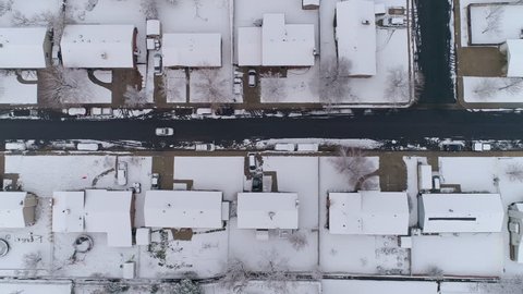 Aerial view looking down at houses and street durning winter as snow covers the neighborhood.