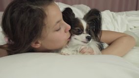 Happy teen girl kisses and plays with dog Papillon in the bed stock footage video