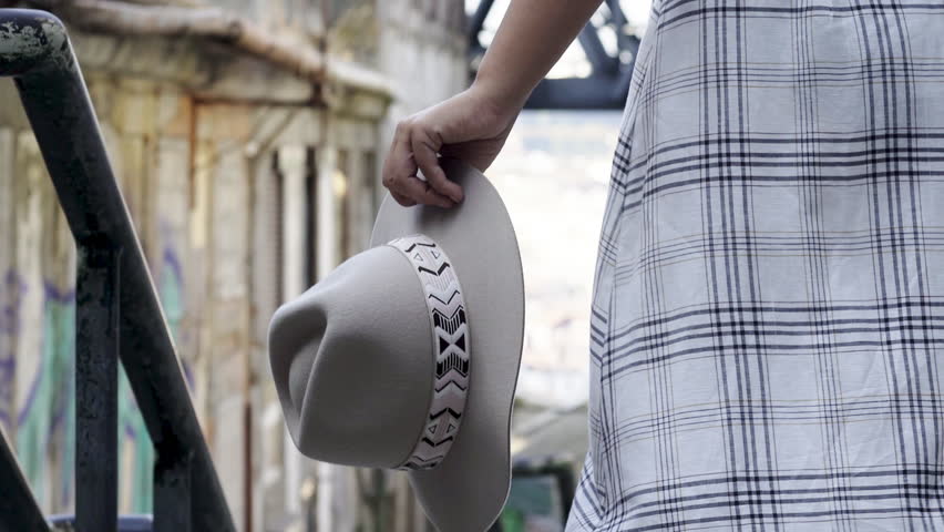 Young lady in casual wear walking on historic street in old centre of Porto. Following woman detail shot hand holding hat.