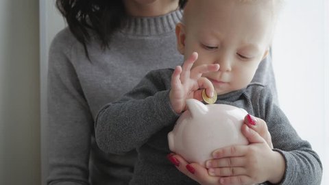 Mother and little son putting coins into piggy bank for the future savings.