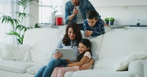 Portrait of happy family having fun using tablet on sofa in living room in slow motion. Shot with RED camera in 8K. Concept of  family entertainment, education, technology