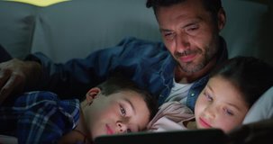 Portrait of happy father and kids using a tablet on sofa in the evening in slow motion. Shot with RED camera in 8K. Concept of family entertainment, education, technology
