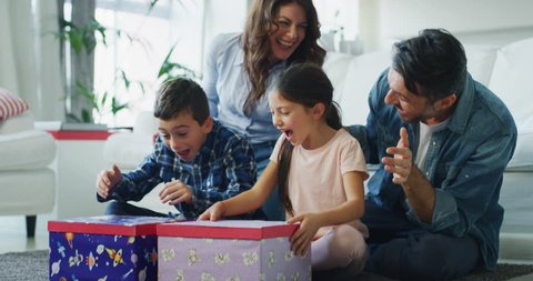 Portrait of happy family having fun to opening presents in living room in slow motion. Shot with RED camera in 8K. Concept of surprise present, birthday gift, happy family, childhood, parenthood