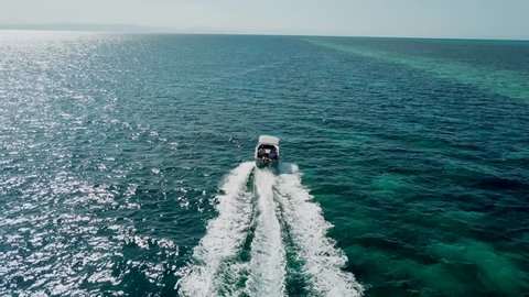 2 men in a small boat driving over a section of the Great Barrier Reef (Tracked by drone)