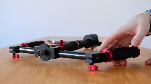Hands of a male videographer are testing the convenience of a new innovative three-axis stabilizer for capturing video lying on a wooden table. Concept of new generation equipment