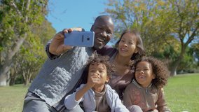Happy Multiethnic family taking selfie on smartphone in summer park in slow motion. Interracial family with kids having video call on digital device. Communication concept